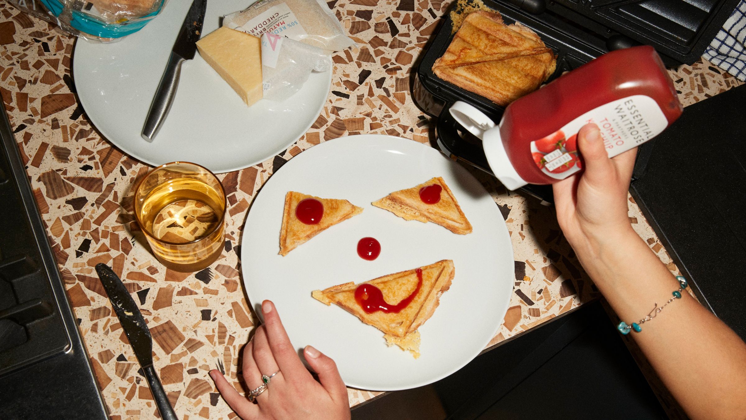 Image of a toastie maker and a student painting smily faces with ketchup on their cheese toastie