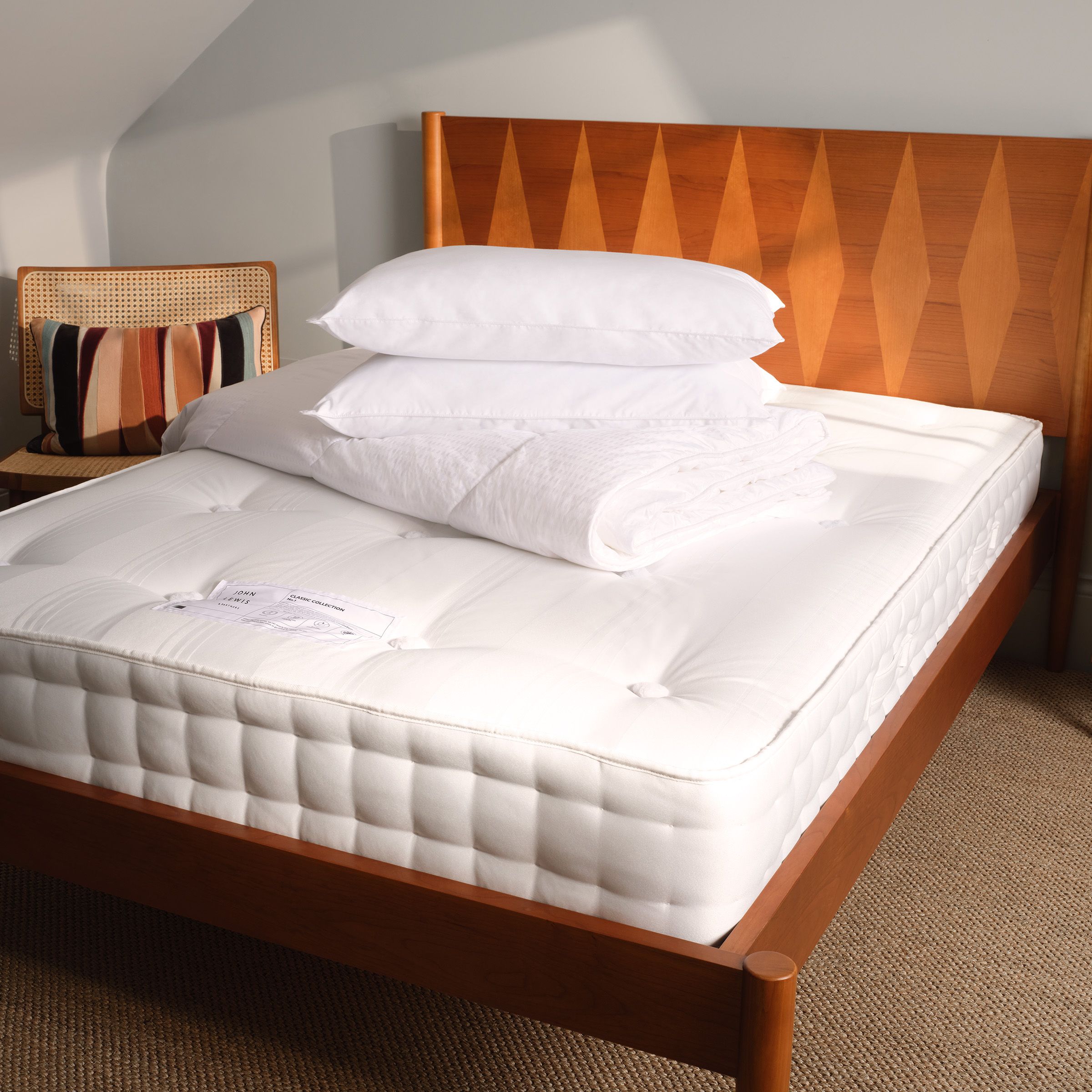 Brown bed frame with white mattress, white cushions and white duvet