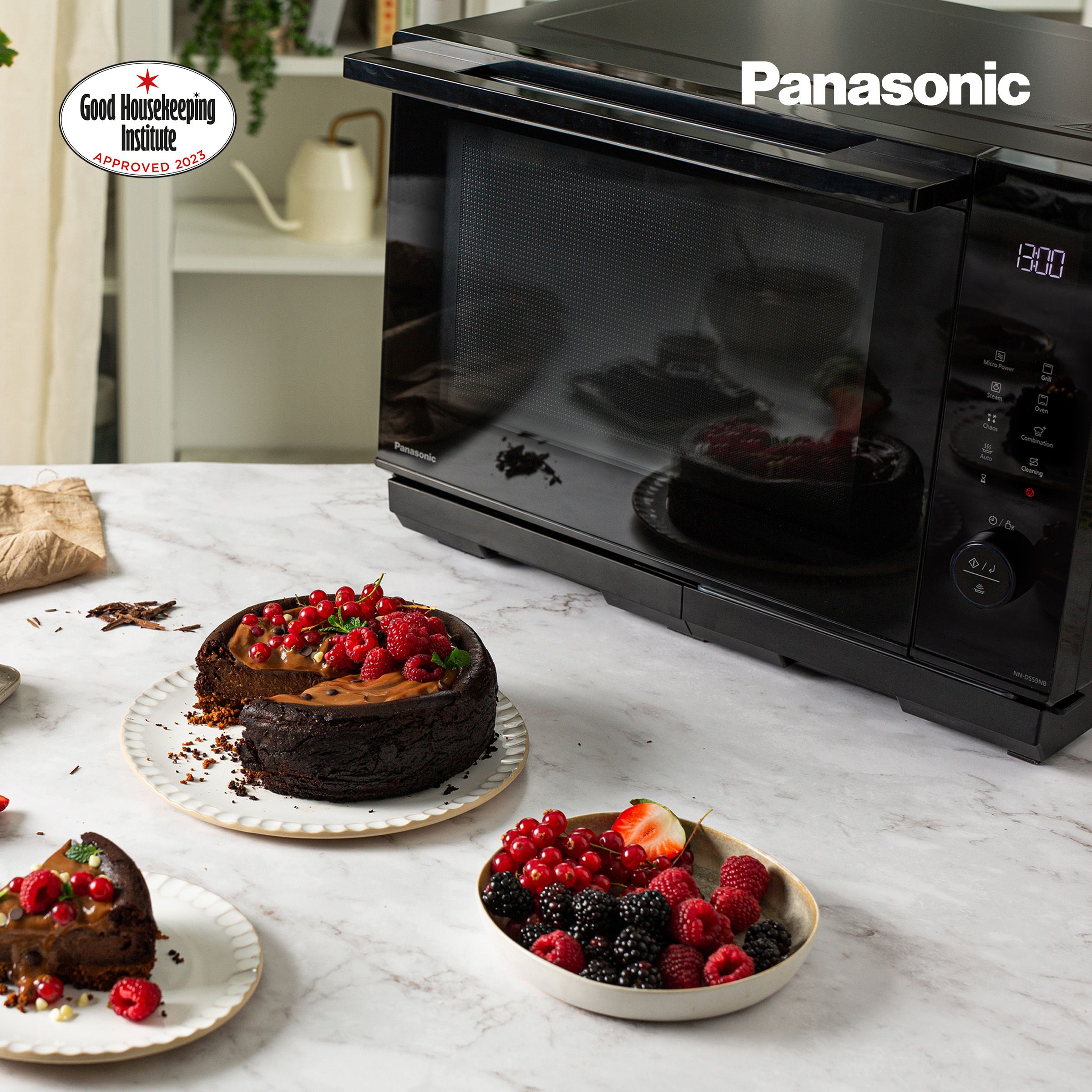 panasonic microwave sittting on a kitchen counter with a big chocolate cake and strawberries in front of it
