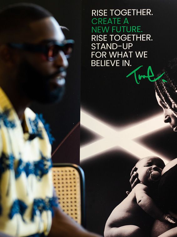 Image of Tinie Tempah next to the sign that says 'Rise together, create a new future. Rise together, stand-up for what we believe in'