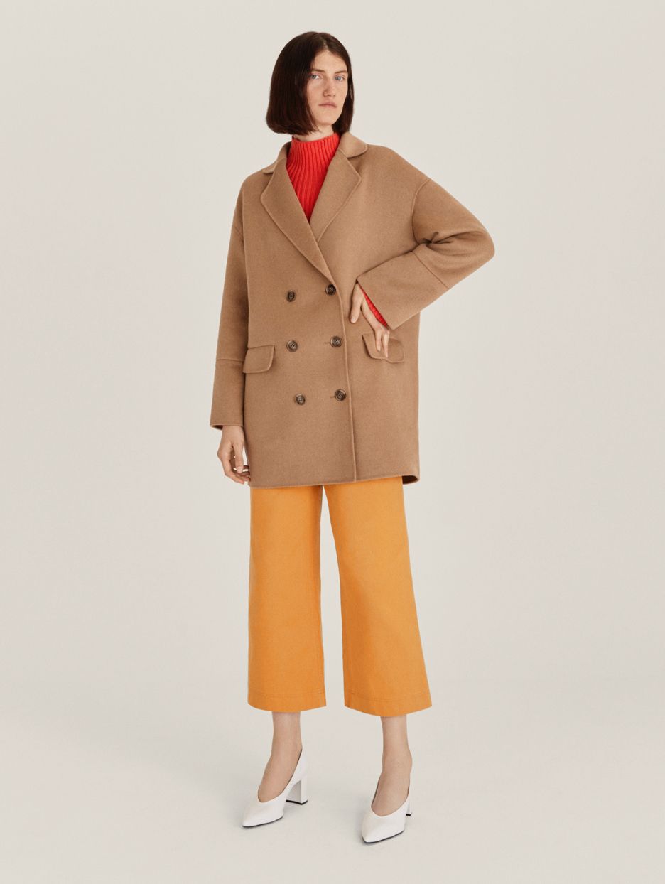 Model wearing camel coat and mustard wide-legged cropped trousers