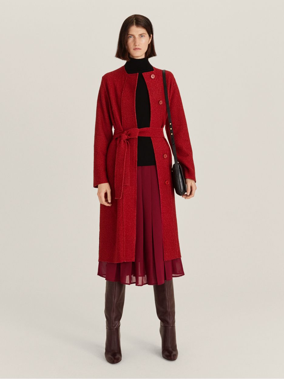 Model wearing red coat and pleated skirt