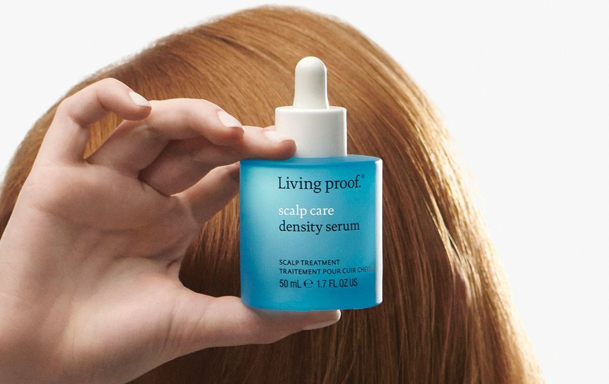 Red haired woman holding Living Proof density infusion cream