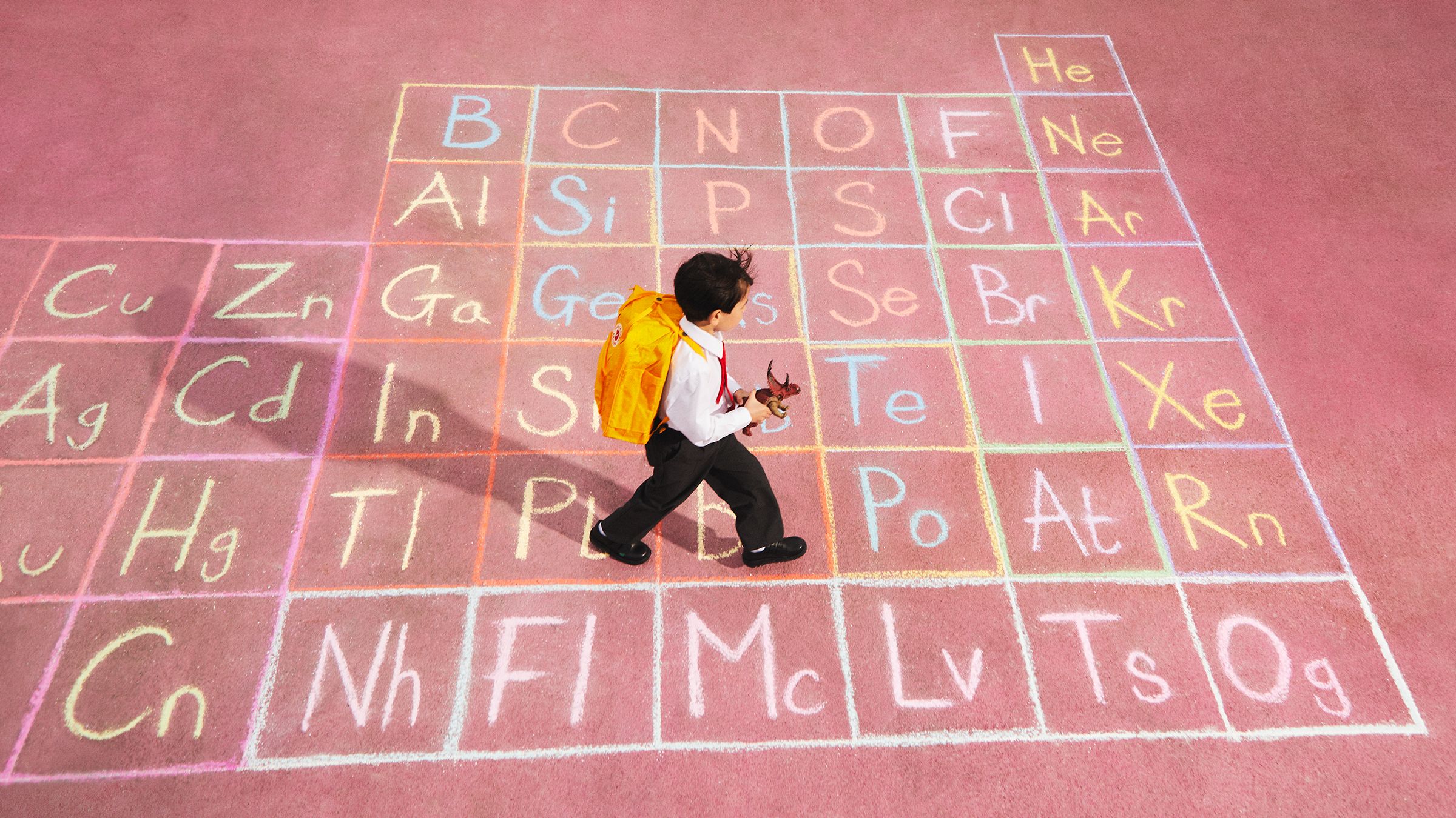 Image of a boy running across the playground with a periodic table in chalk on the floor