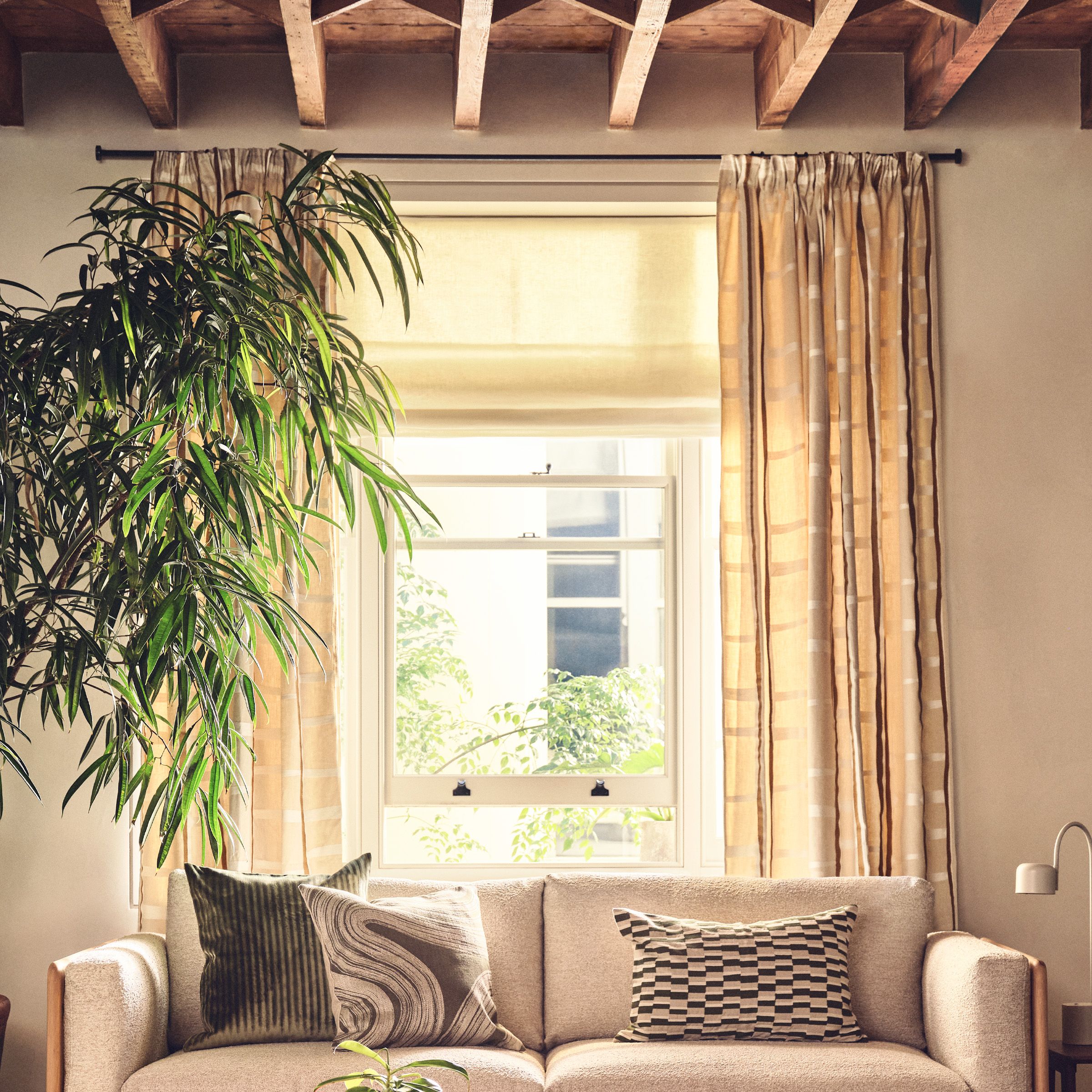 neutral curtains framing a wooden window behind a sofa