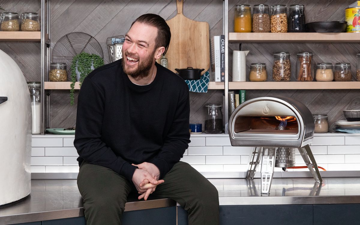 Image of Tom Gozney sitting on a kicthen counter with one of his pizza ovens