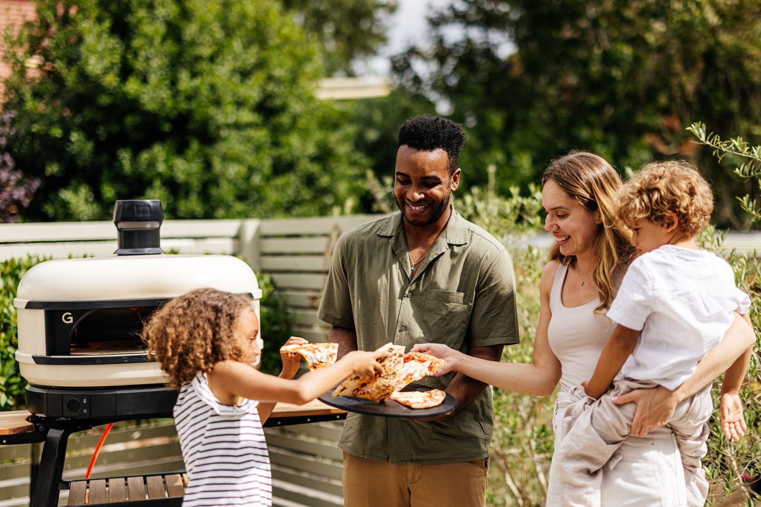 Image of a gas Gozney pizza oven with a family around it taking their pizza out