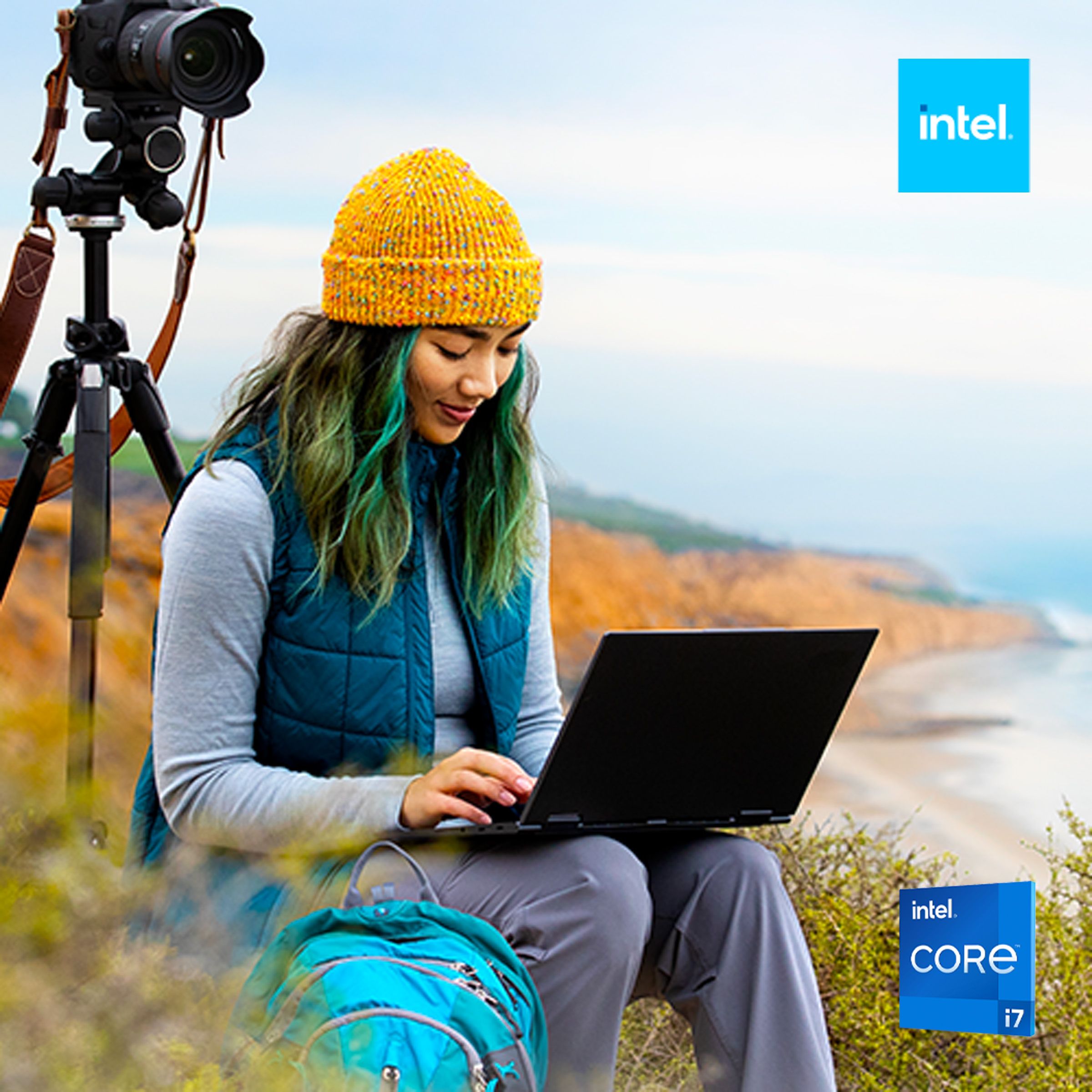 Woman sitting on coastal hillside next to camera in tripod with Intel Core laptop