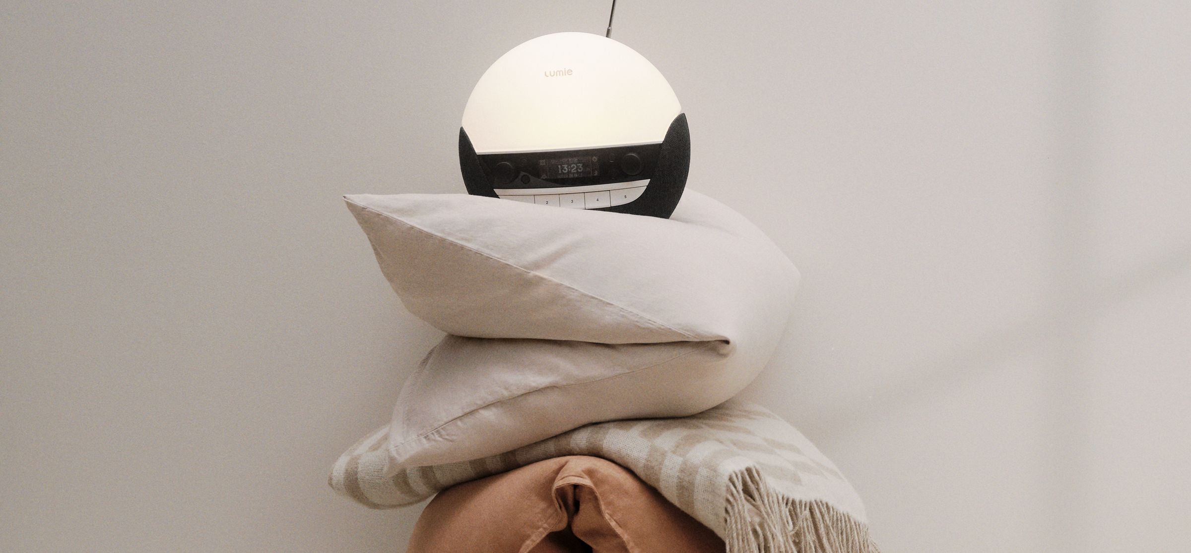 Image of a Lumie Alarm Clock stacked on top of some duvets with a beige background