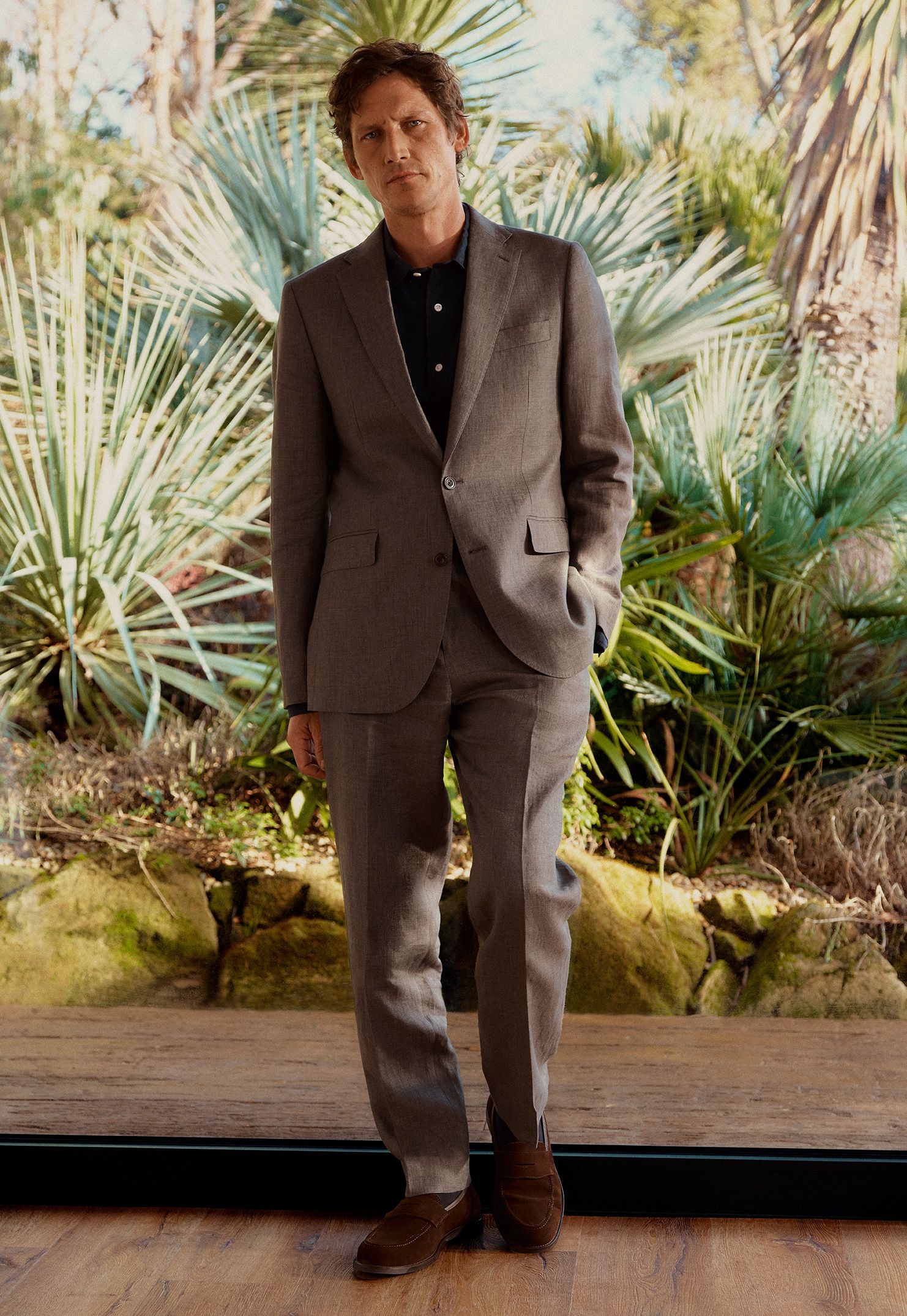 Image of a man in a tailored suit standing in-front of a jungle background