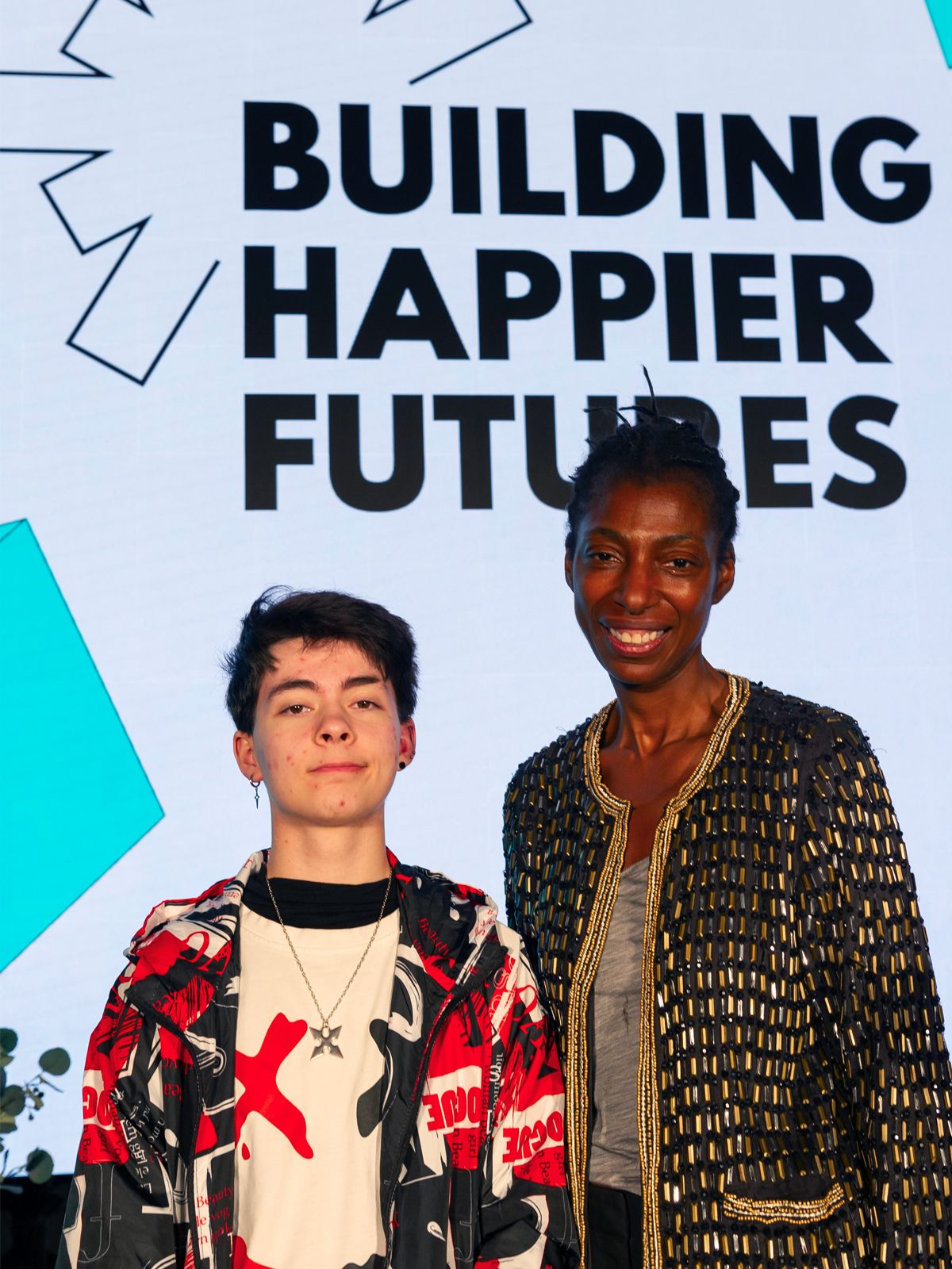 An image of Michael and Sharon standing in-front of the Happier Brighter Futures logo on the wall