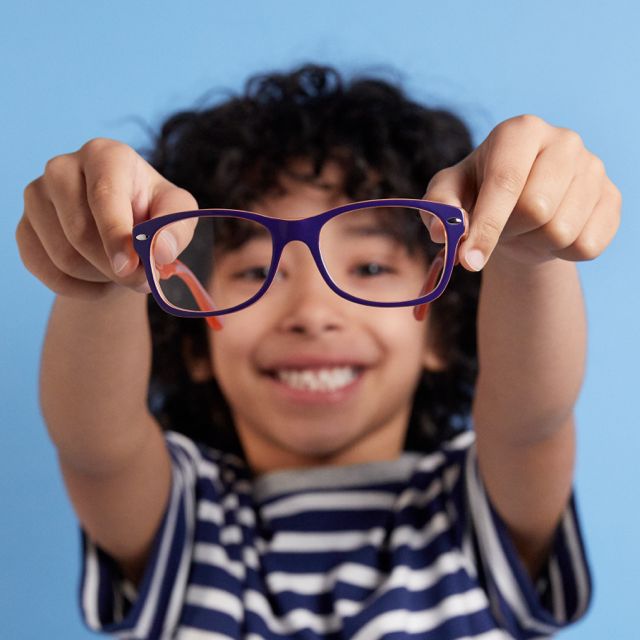 Boy out of focus on a blue background holding up glasses in focus