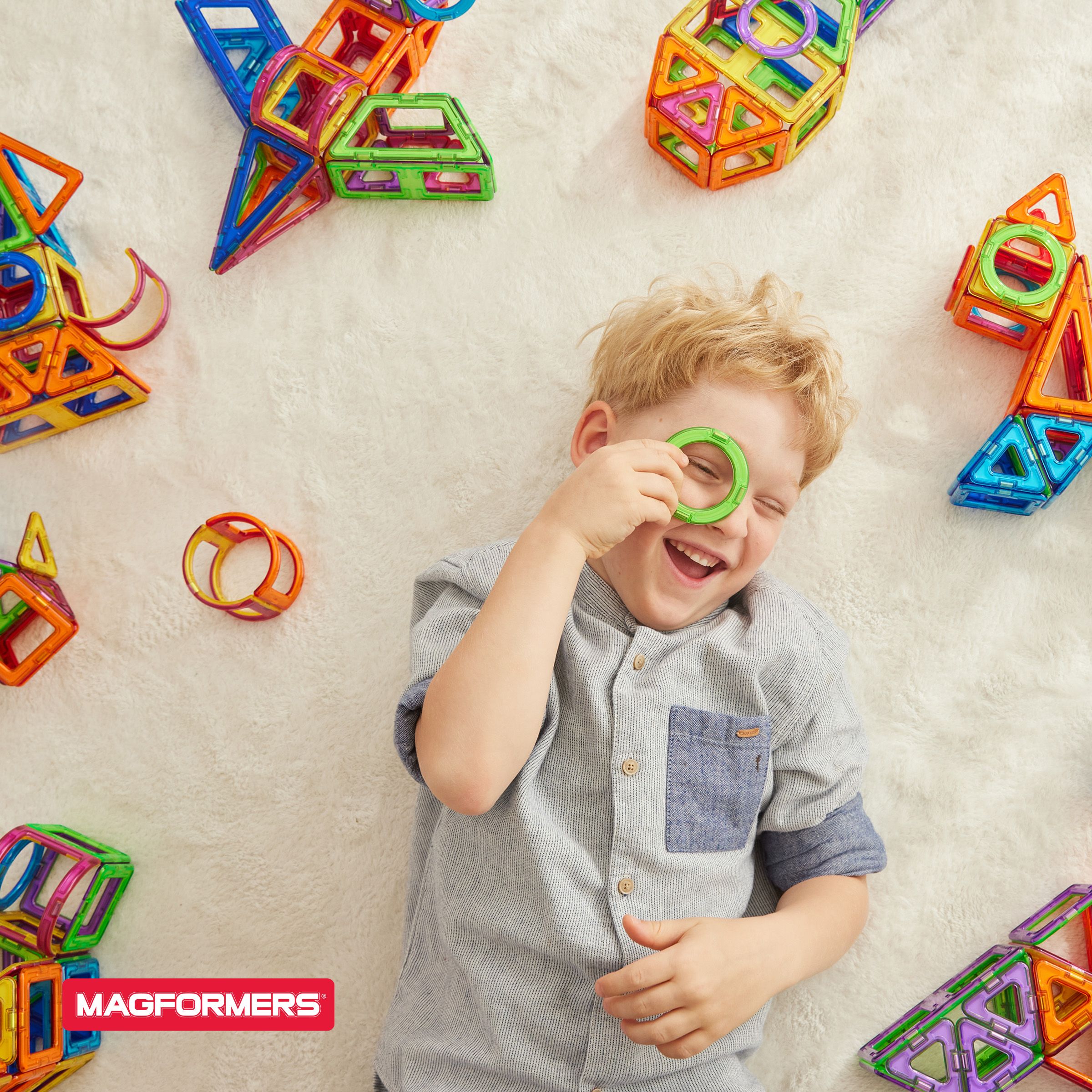 Shop Magformers child laying on the floor with magnetic toys laughing and smiling