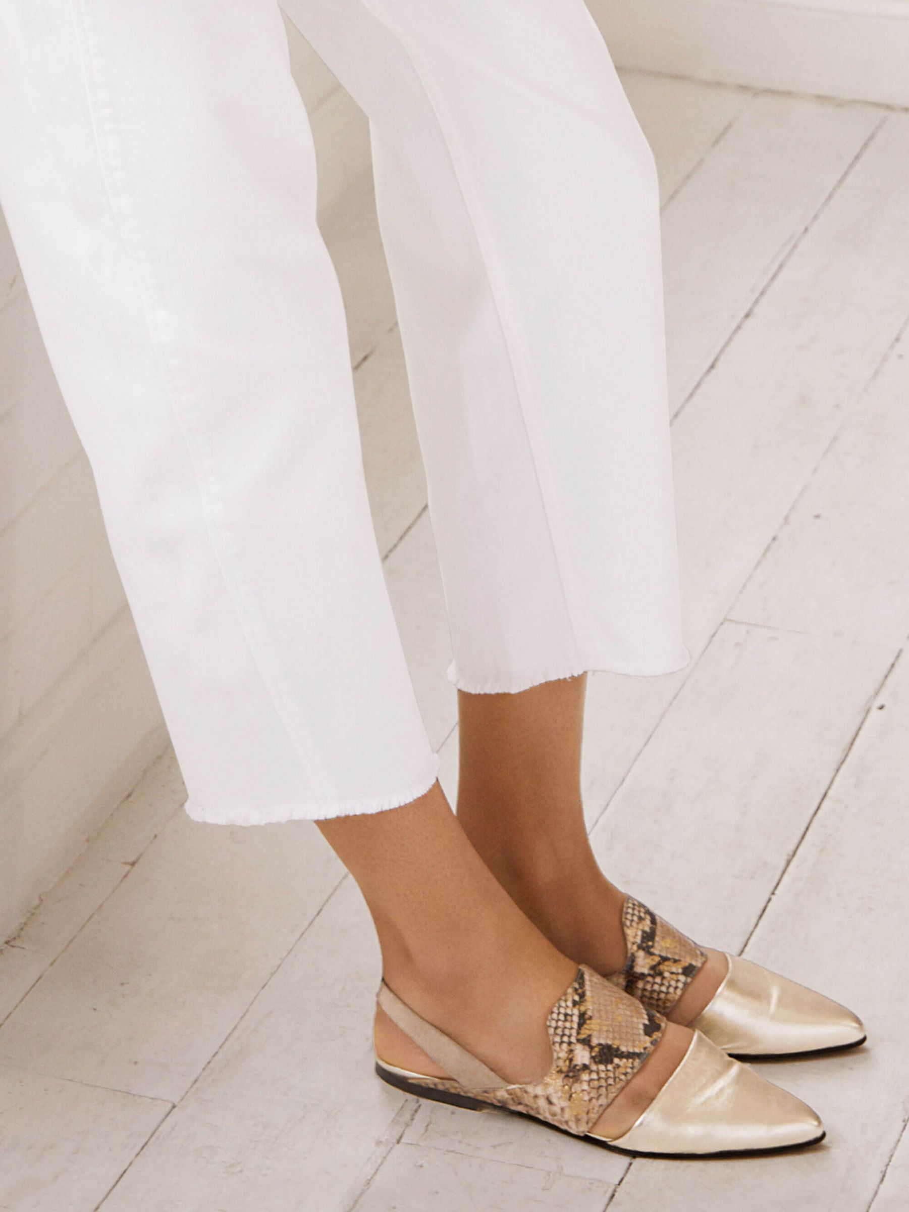 Woman wearing white cropped jeans and gold flat shoes
