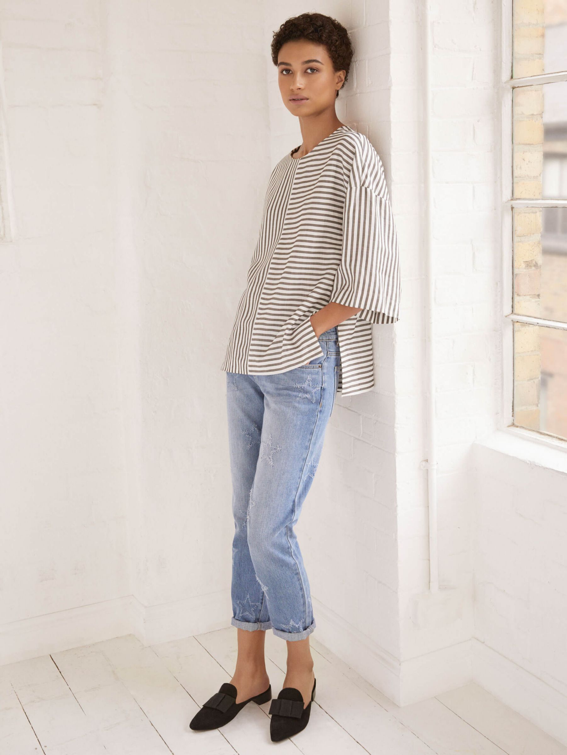 Woman leaning against a wall in blue jeans and a striped top